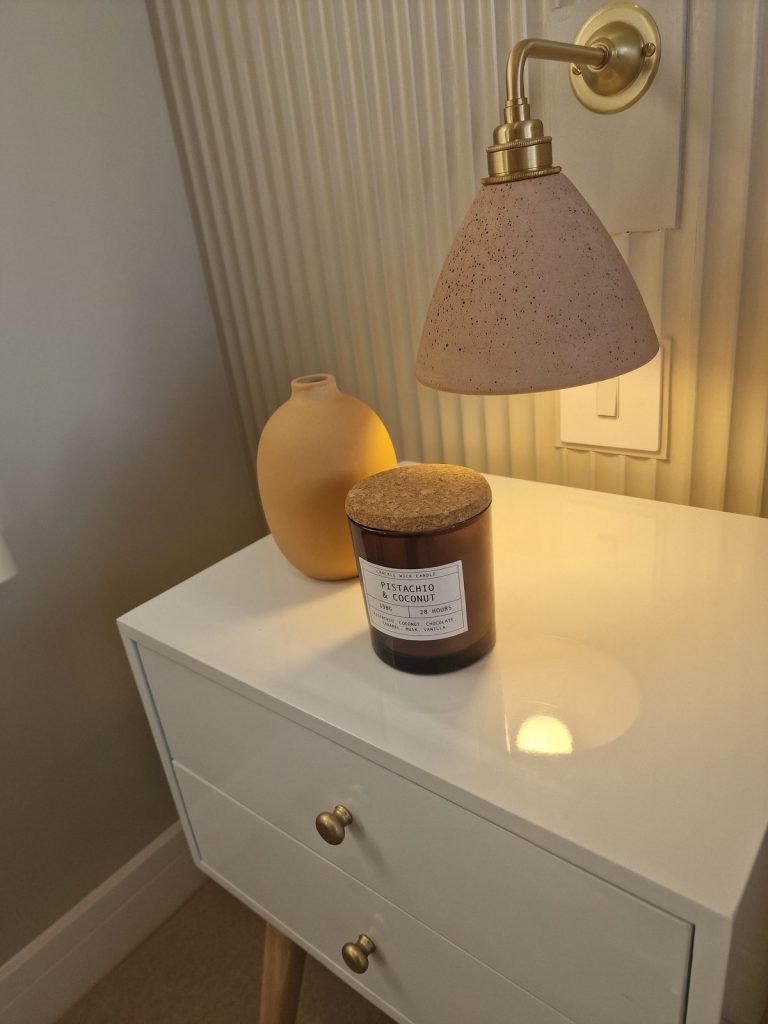 White bedside table with a candle, ochre vase and a speckled wall lamp